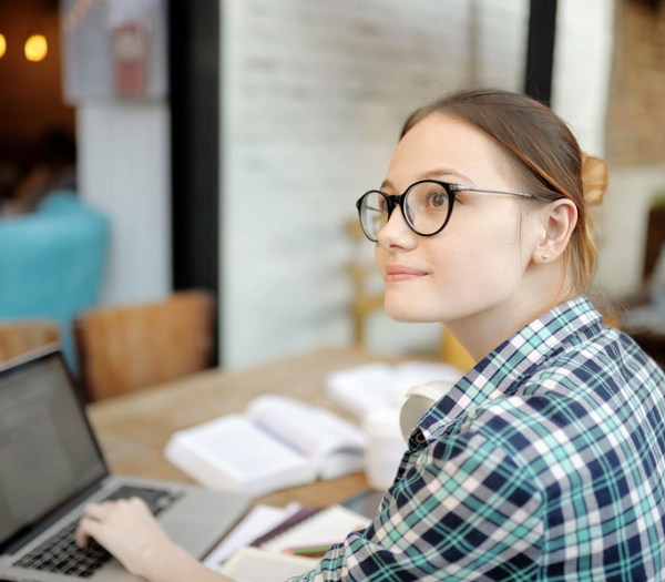 Young caucasian woman wearing glasses sitting at table with open books and laptop